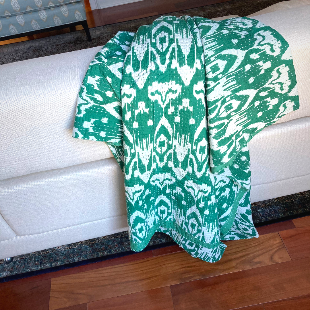 Handmade green and white ikat design Kantha blanket draped over a white sofa with wooden floor background